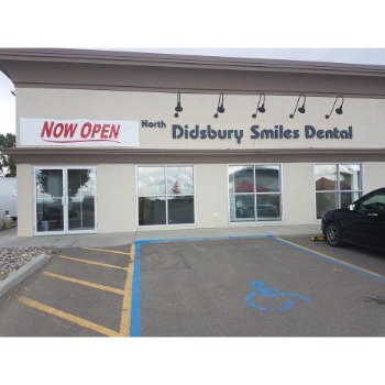 Front of North Pidsbury Smiles Dental clinic with a 'NOW OPEN' banner, large front windows, and a parking lot featuring a handicap space in blue with a parked car nearby.