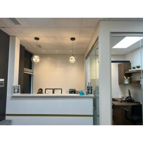 Reception desk in a modern office with a white counter, two pendant lights, and a glass doorway on the right.