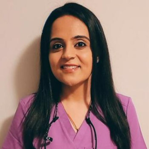 Smiling female healthcare professional in purple scrubs with a stethoscope around her neck, facing the camera.