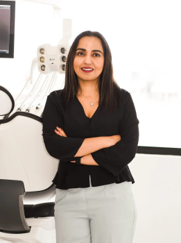 Professional woman with arms crossed in a bright clinic, medical equipment visible behind her.