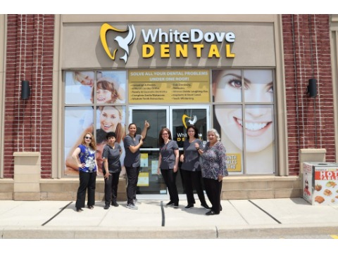 Group of seven dental staff standing in front of White Dove Dental storefront, posing for a photo outside the clinic.