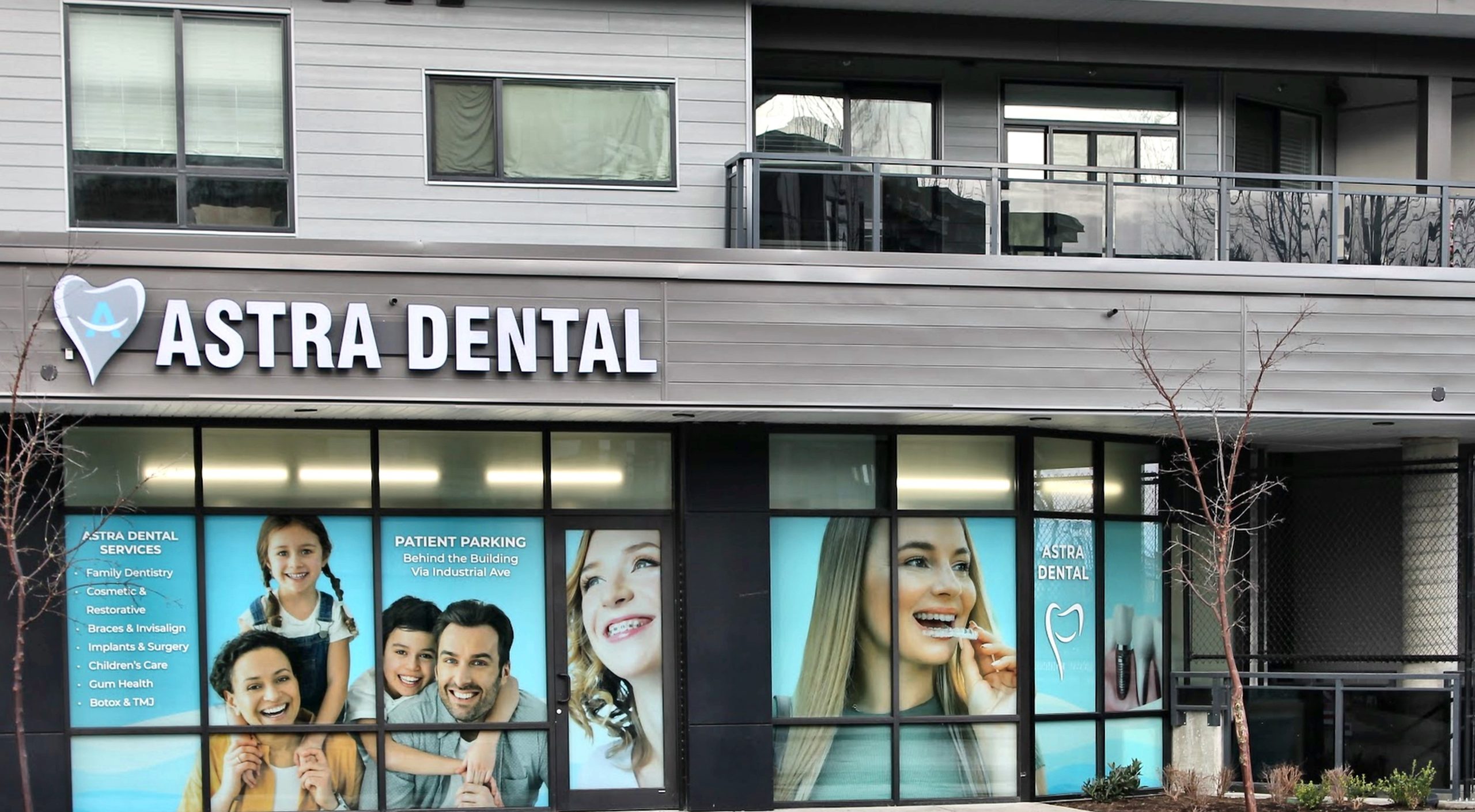 Astra Dental storefront with large glass windows and bold white signage, blue tooth logo on the left, displaying patient posters in teal panels behind glass.