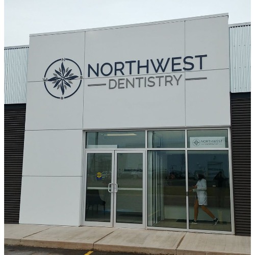 Facade of Northwest Dentistry clinic storefront with logo and sign; glass double doors and a person walking inside.