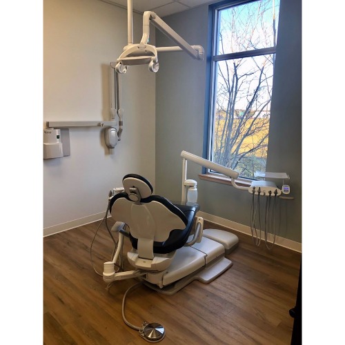 Dental treatment chair with overhead light and mounted dental tools in a clean clinic room by a window with a view of trees outside