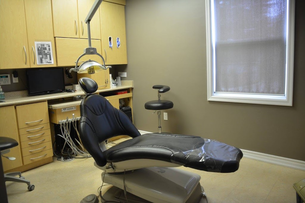 Dental clinic operatory with a black reclining chair, overhead light, and wooden cabinets.
