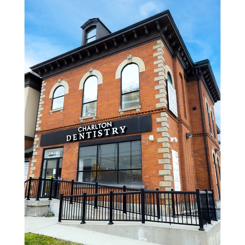 Brick two-story dentistry office with a black Charlton Dentistry sign and arched windows under a blue sky, metal railing at the entrance.