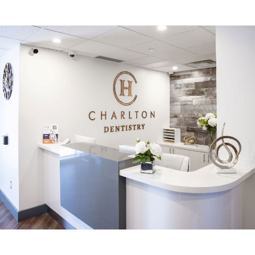 Front desk of Charlton Dentistry reception with a white curved counter and the Charlton logo on the wall behind it.