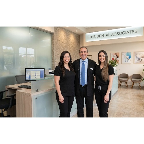 Three dental professionals stand together in the reception area of The Dental Associates, smiling at the camera.