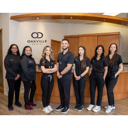Group of seven dental staff in black scrubs posing in the Oakville Dental reception area, smiling at the camera.