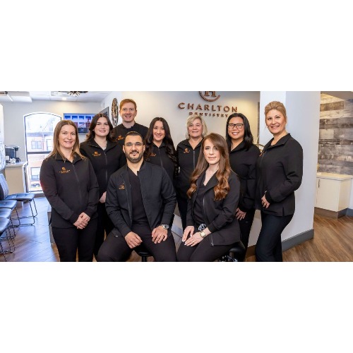 Group portrait of nine staff members in black uniforms posing in a Charlton Branch salon reception, smiling at the camera.