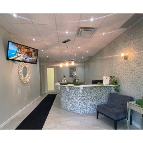 Reception lobby with a curved mosaic-front desk, gray patterned walls, a dark bench, and a wall-mounted TV