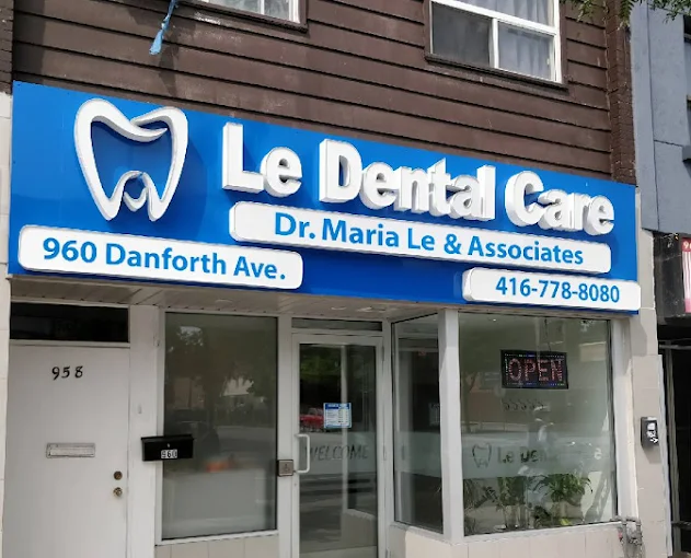 Front of a dental clinic storefront with a bright blue sign reading 'Le Dental Care' and 'Dr. Maria Le & Associates'; visible address 960 Danforth Ave and phone number 416-778-8080; OPEN sign in window.
